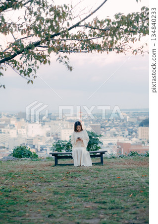 A Japanese woman looking at her smartphone on a hill overlooking the cityscape 134840233