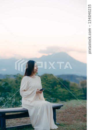 一位日本女子站在俯瞰城市景觀的山坡上，看著她的智慧型手機。 134840235