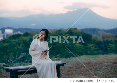 A Japanese woman looking at her smartphone on a hill overlooking the cityscape 134840239