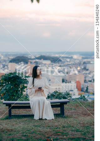 一位日本女子站在俯瞰城市景觀的山坡上,看著她的智慧型手機。 一位日本女子站在俯瞰城市景觀的山坡上,看著她的智慧型手機。 134840240