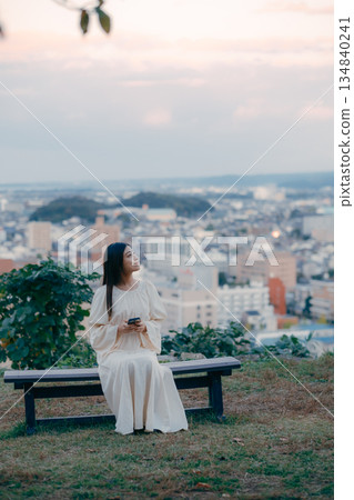 A Japanese woman looking at her smartphone on a hill overlooking the cityscape 134840241