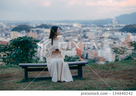 A Japanese woman looking at her smartphone on a hill overlooking the cityscape A Japanese woman looking at her smartphone on a hill overlooking the cityscape 134840242