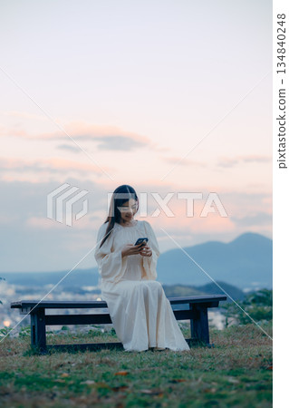A Japanese woman looking at her smartphone on a hill overlooking the cityscape A Japanese woman looking at her smartphone on a hill overlooking the cityscape 134840248