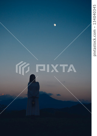 Silhouette of a woman standing in the mountains at sunset with the moon rising Silhouette of a woman standing in the mountains at sunset with the moon rising 134840345
