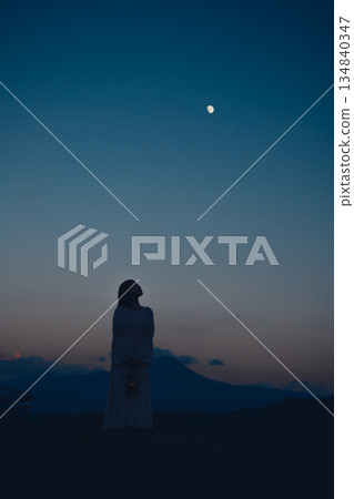 夕陽西下，月亮升起，一位女子的身影佇立在山間。 134840347