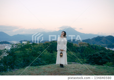 A woman standing with a lantern at sunset in the mountains 134840380