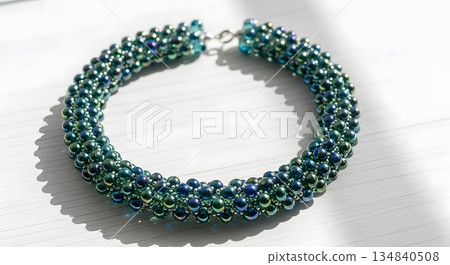 Iridescent Teal And Blue Beaded Bracelet On White Surface Displaying Intricate Design And Craftsmanship Iridescent Teal And Blue Beaded Bracelet On White Surface Displaying Intricate Design And Craftsmanship 134840508