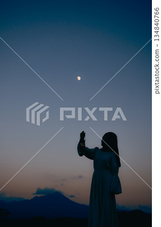 夕陽西下,月亮升起,一位女子的身影佇立在山間。 夕陽西下,月亮升起,一位女子的身影佇立在山間。 134840766