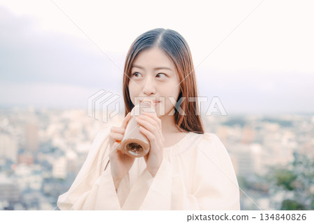 Woman drinking tea with city in the background Woman drinking tea with city in the background 134840826