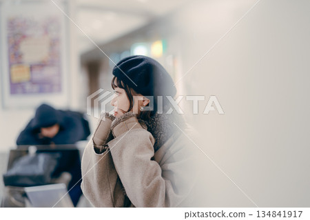 一位三十多歲的女性坐在那裡,一邊使用智慧型手機一邊等待預約。 一位三十多歲的女性坐在那裡,一邊使用智慧型手機一邊等待預約。 134841917