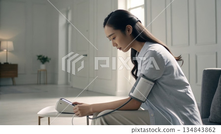 Young woman measuring blood pressure at home with a digital device 134843862
