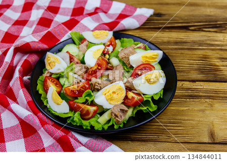 Tasty tuna salad with eggs, lettuce and fresh vegetables on wooden table 134844011
