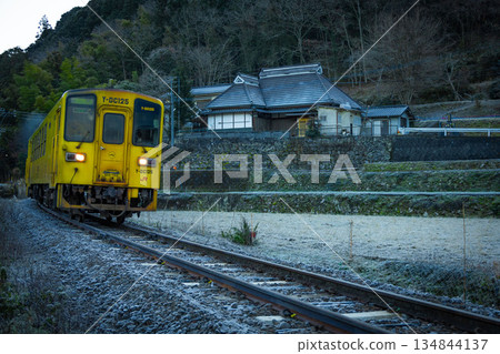 Yellow local train running alongside an old house 134844137