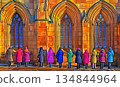 Colorful Coats Before Stained Glass: A Row of Onlookers at a Got 134844964