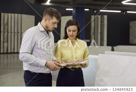 Young couple choosing tile looking at samples standing at building market planning repair in house Young couple choosing tile looking at samples standing at building market planning repair in house 134845923