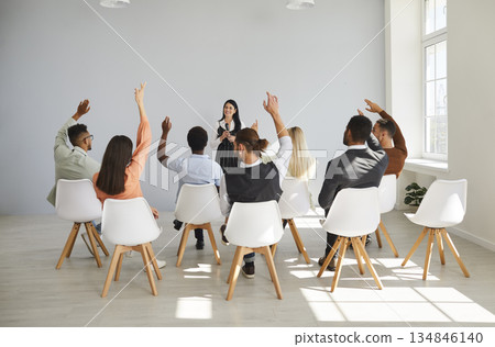 Audience raising hands in business seminar as presenter leads group training Audience raising hands in business seminar as presenter leads group training 134846140