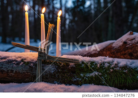 Blessed Imbolc greeting card. Brigid cross of straw and candles. Winter forest nature background. symbol of Imbolc Blessed Imbolc greeting card. Brigid cross of straw and candles. Winter forest nature background. symbol of Imbolc 134847276