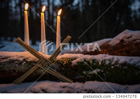 Blessed Imbolc greeting card. Brigid cross of straw and candles. Winter forest nature background. symbol of Imbolc Blessed Imbolc greeting card. Brigid cross of straw and candles. Winter forest nature background. symbol of Imbolc 134847278
