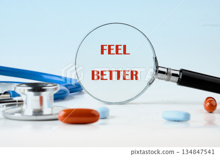 A magnifying glass highlights the words Feel Better next to a stethoscope and scattered pills, presenting a message of healing and recovery 134847541