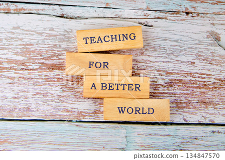 Wooden blocks displaying the words Teaching For A Better World are stacked on a weathered surface. The background is painted light blue and beige 134847570