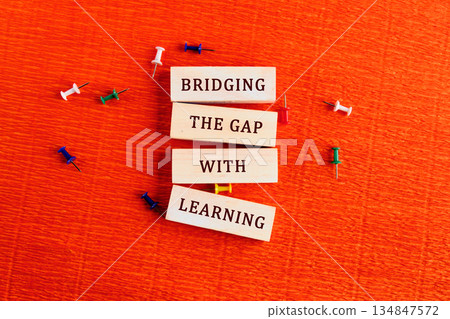 Wooden blocks show phrases about learning, pinned down by colorful push pins. These educational concepts suggest building up skills on an orange textured surface 134847572