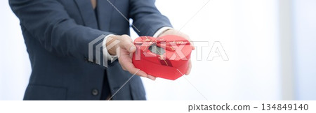 Smiling businessman holding a heart-shaped gift, Valentine's Day gift, no face, hands Smiling businessman holding a heart-shaped gift, Valentine's Day gift, no face, hands 134849140