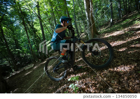 Mountain rider conquering a forest trail on an electric mountain bike in bright dappled light Mountain rider conquering a forest trail on an electric mountain bike in bright dappled light 134850050