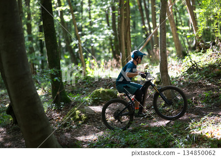 Person rides an electric mountain bike through a sunlit forest trail wearing a helmet Person rides an electric mountain bike through a sunlit forest trail wearing a helmet 134850062