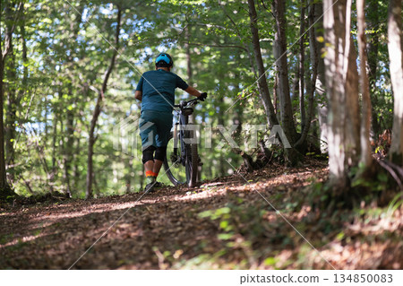 Mountain biker pushes through a forest trail on a sunny day wearing helmet and gear Mountain biker pushes through a forest trail on a sunny day wearing helmet and gear 134850083