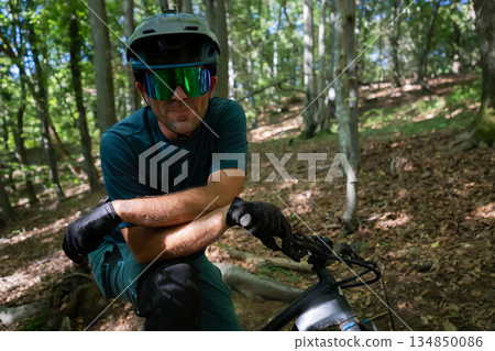 Man riding an electric mountain bike through a forest trail wearing helmet and gloves 134850086