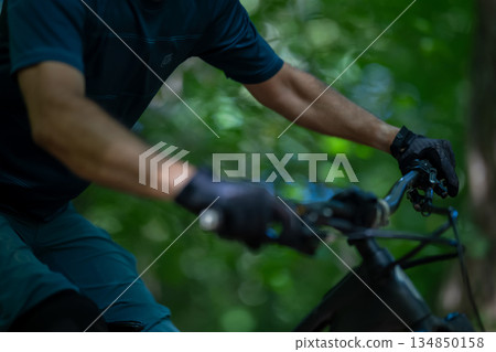 Cyclist riding an electric mountain bike through a lush forest trail focusing on the handlebars 134850158