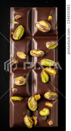 Dark chocolate bar with pistachios creating sweet gourmet dessert 134850361