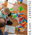 Parent assisting a child with a colorful toy track and instruction booklet. The scene shows learning, cooperation, creativity, and a supportive family atmosphere at home. 134850702