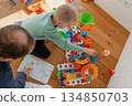 Parent and child assembling a colorful toy construction set on the floor. Shared playtime reflects family bonding, learning, creativity, and a warm home environment 134850703