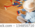Young child assembling a tall structure from colorful building blocks on a wooden floor. Focused play and bright elements highlight childhood development, creativity, problem-solving and imaginative 134850710