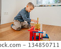 Young child sitting on the floor and assembling colorful building blocks. Calm home environment and focused play highlight themes of childhood development, creativity, motor skills and learning 134850711