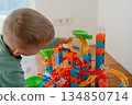 Young child playing with a colorful construction toy set on the floor. Bright pieces and concentrated activity evoke themes of learning, creativity, childhood, and home life. 134850714
