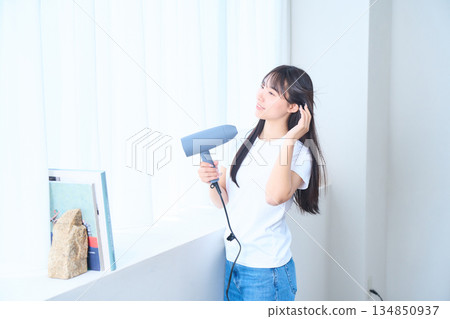 A Japanese woman using a hair dryer in a bright living room A Japanese woman using a hair dryer in a bright living room 134850937