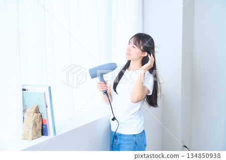 A Japanese woman using a hair dryer in a bright living room A Japanese woman using a hair dryer in a bright living room 134850938