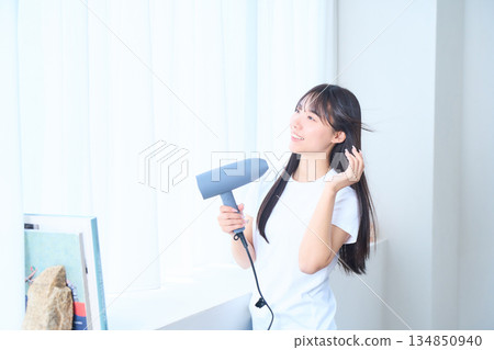 A Japanese woman using a hair dryer in a bright living room A Japanese woman using a hair dryer in a bright living room 134850940