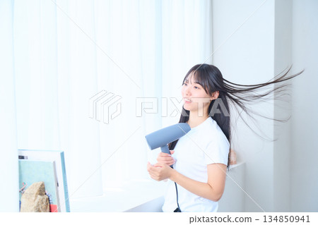 A Japanese woman using a hair dryer in a bright living room A Japanese woman using a hair dryer in a bright living room 134850941