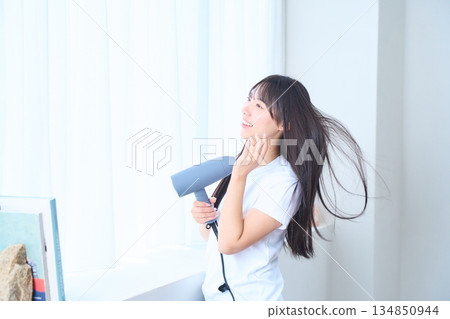 A Japanese woman using a hair dryer in a bright living room A Japanese woman using a hair dryer in a bright living room 134850944