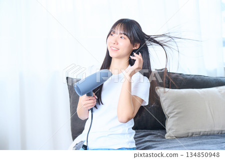 A Japanese woman using a hair dryer in a bright living room 134850948