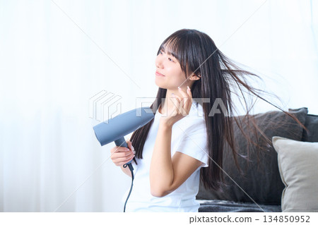 A Japanese woman using a hair dryer in a bright living room 134850952