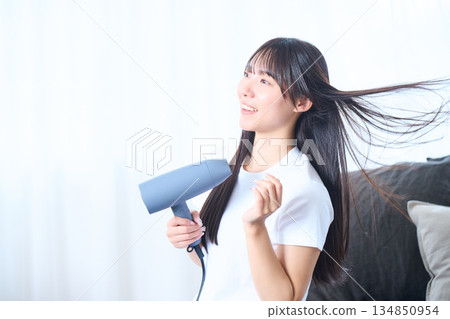 A Japanese woman using a hair dryer in a bright living room A Japanese woman using a hair dryer in a bright living room 134850954