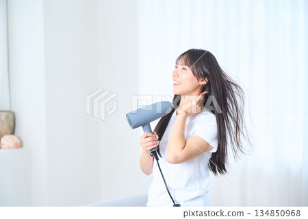 一位日本女性在明亮的客廳使用吹風機 134850968