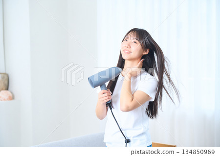 A Japanese woman using a hair dryer in a bright living room A Japanese woman using a hair dryer in a bright living room 134850969