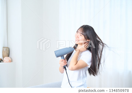 A Japanese woman using a hair dryer in a bright living room A Japanese woman using a hair dryer in a bright living room 134850978