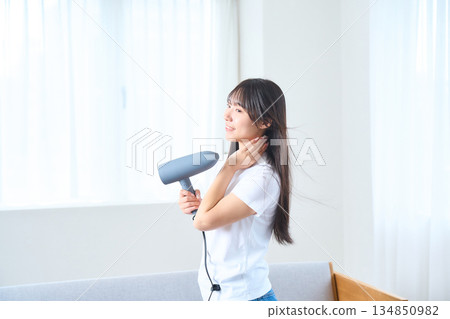 A Japanese woman using a hair dryer in a bright living room 134850982