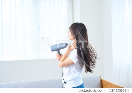 A Japanese woman using a hair dryer in a bright living room 134850984